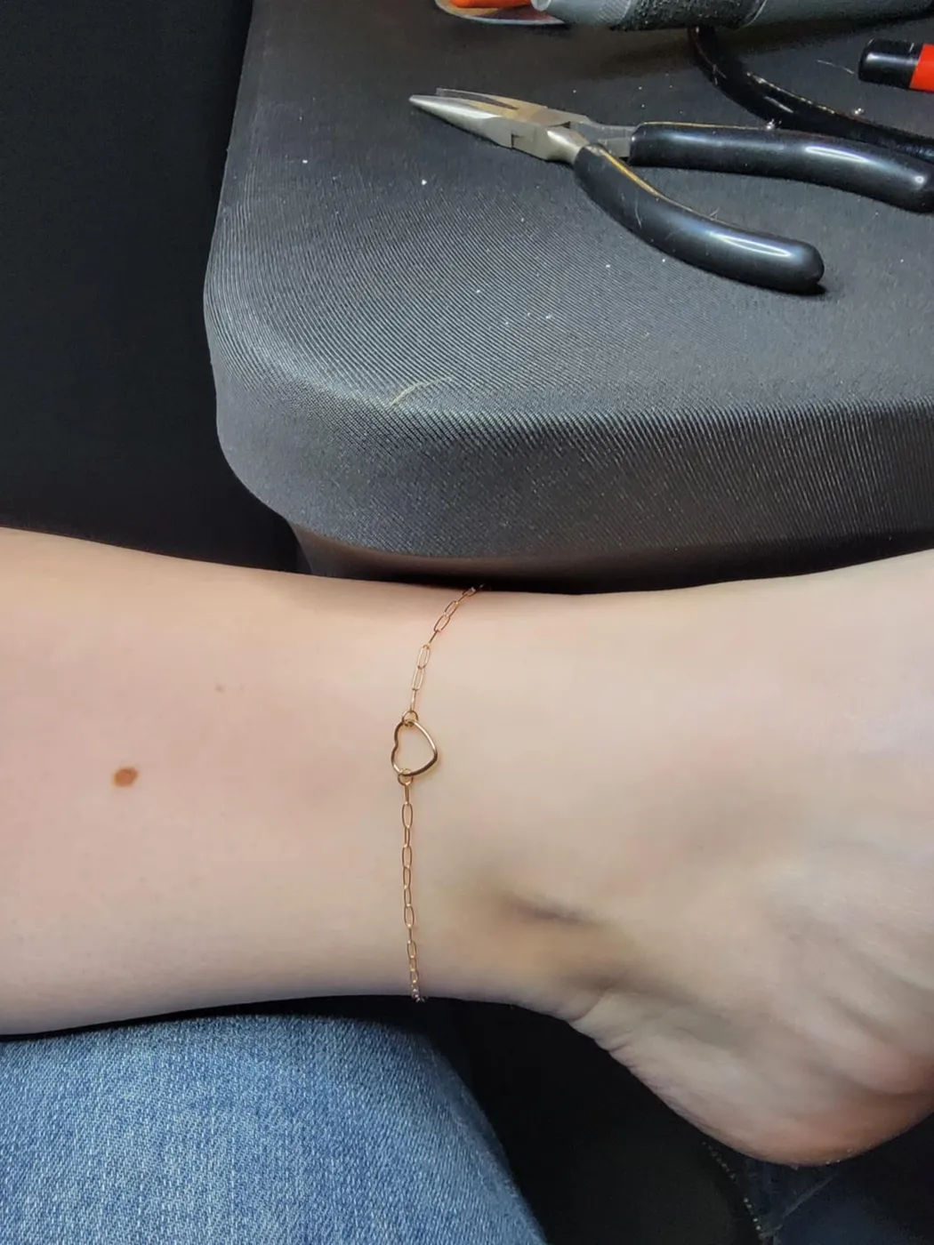 Delicate gold anklet with an open heart link, tools in the background
