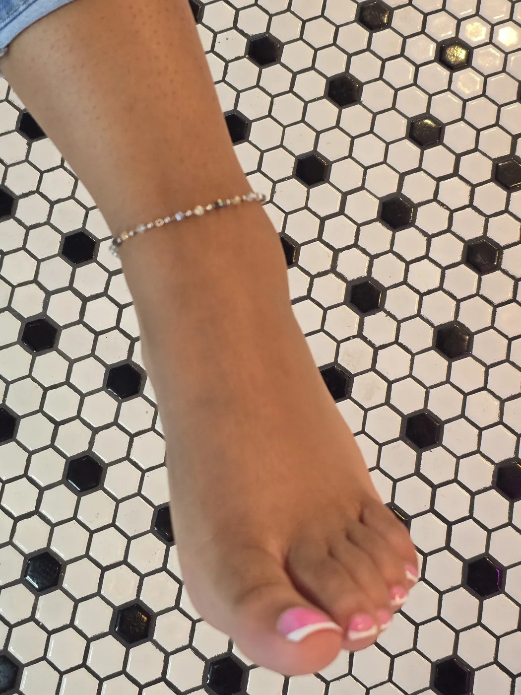 Delicate beaded anklet on a client's ankle over black and white tile