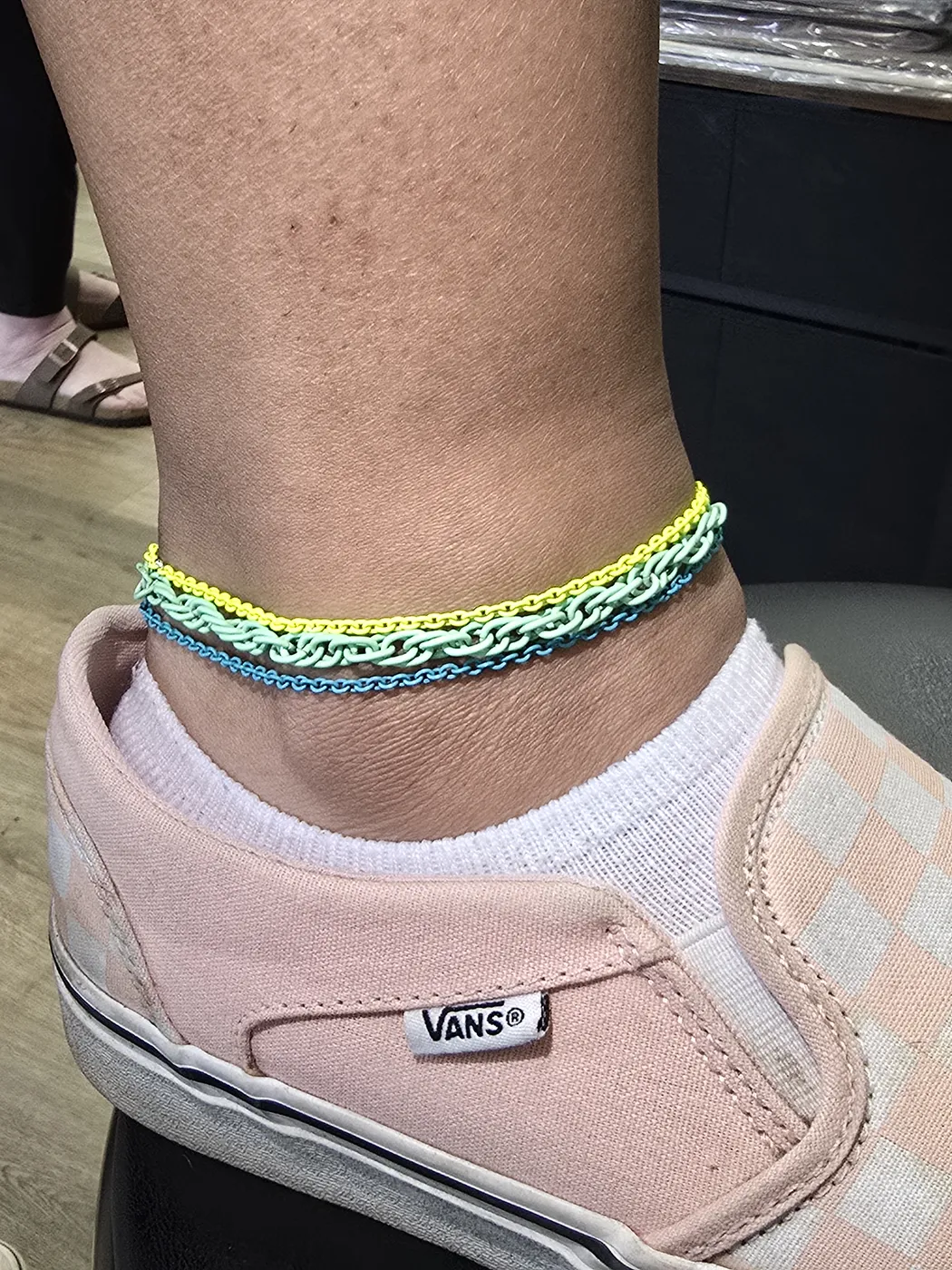 Bright stacked anklets in yellow, teal and blue above a sneaker