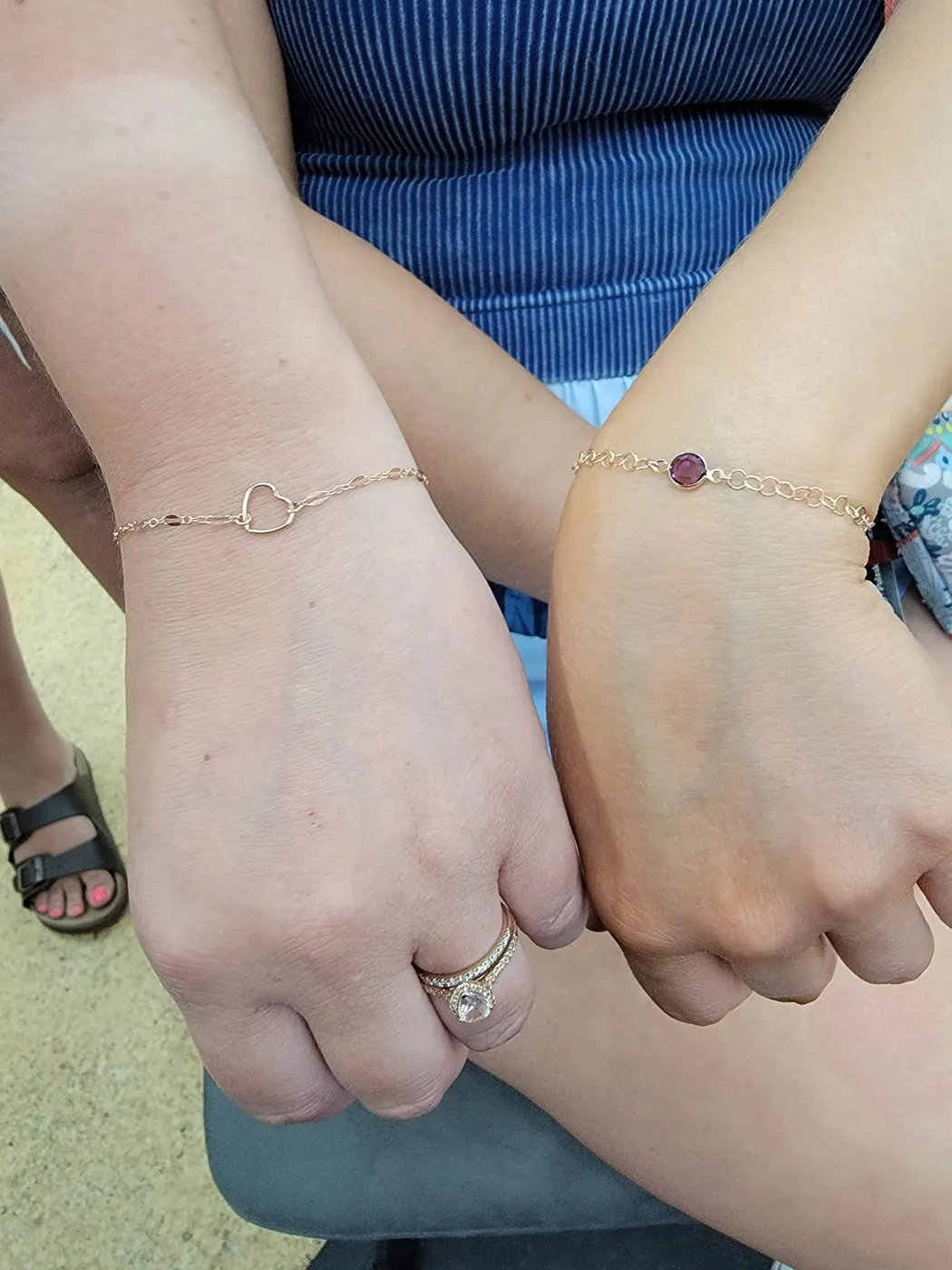 Two wrists side by side wearing matching fine chain bracelets