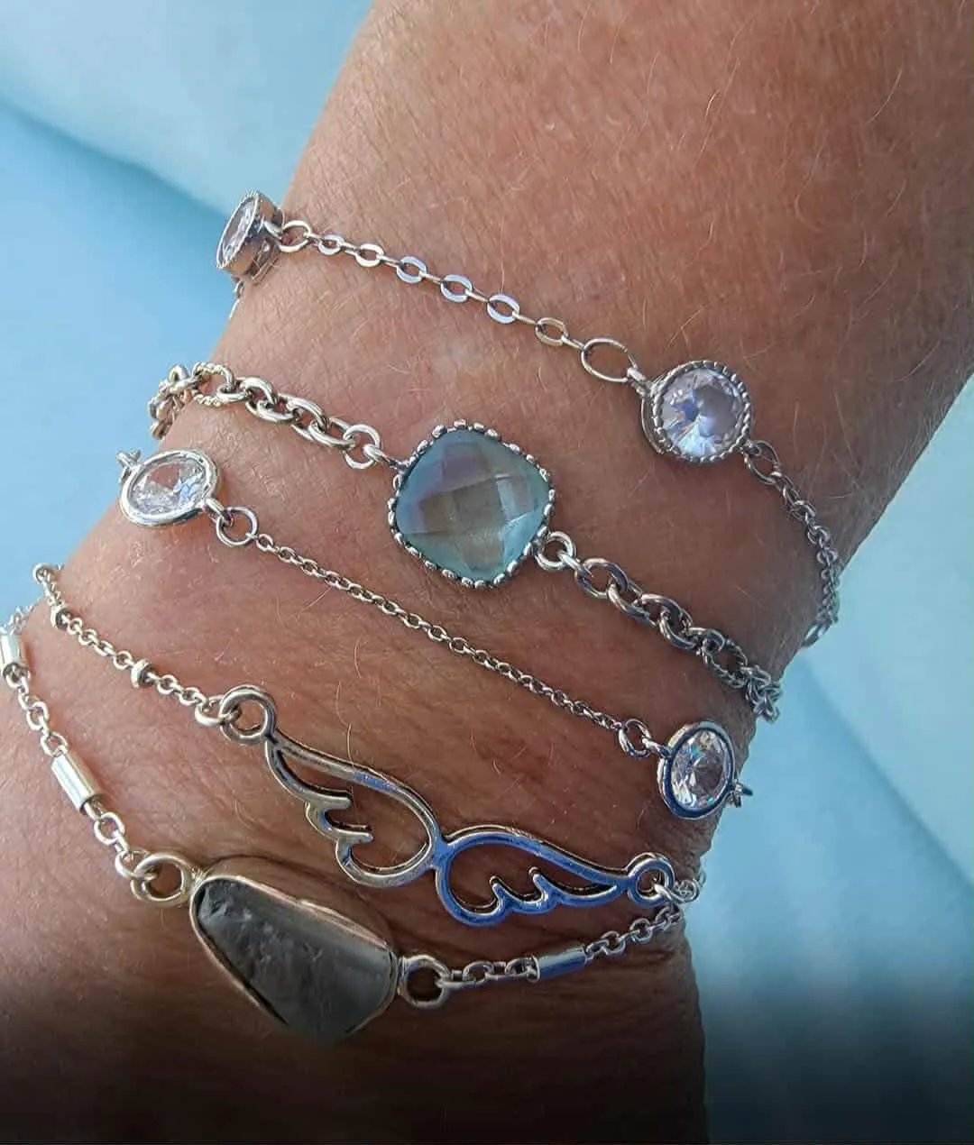 Stack of silver bracelets with crystal and wing details on a wrist