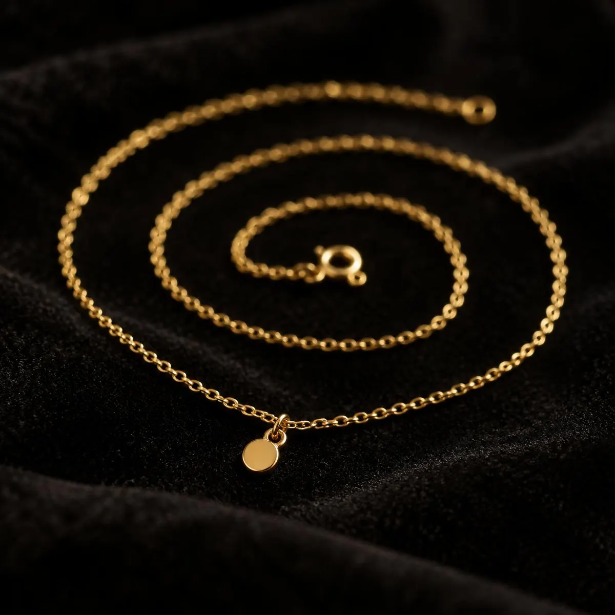 Fine gold chain with a small round charm coiled on black velvet