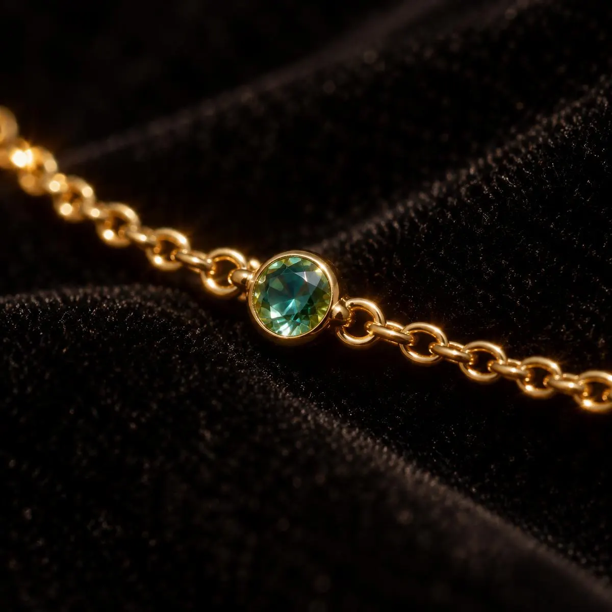 Gold chain with a single green crystal link on black velvet
