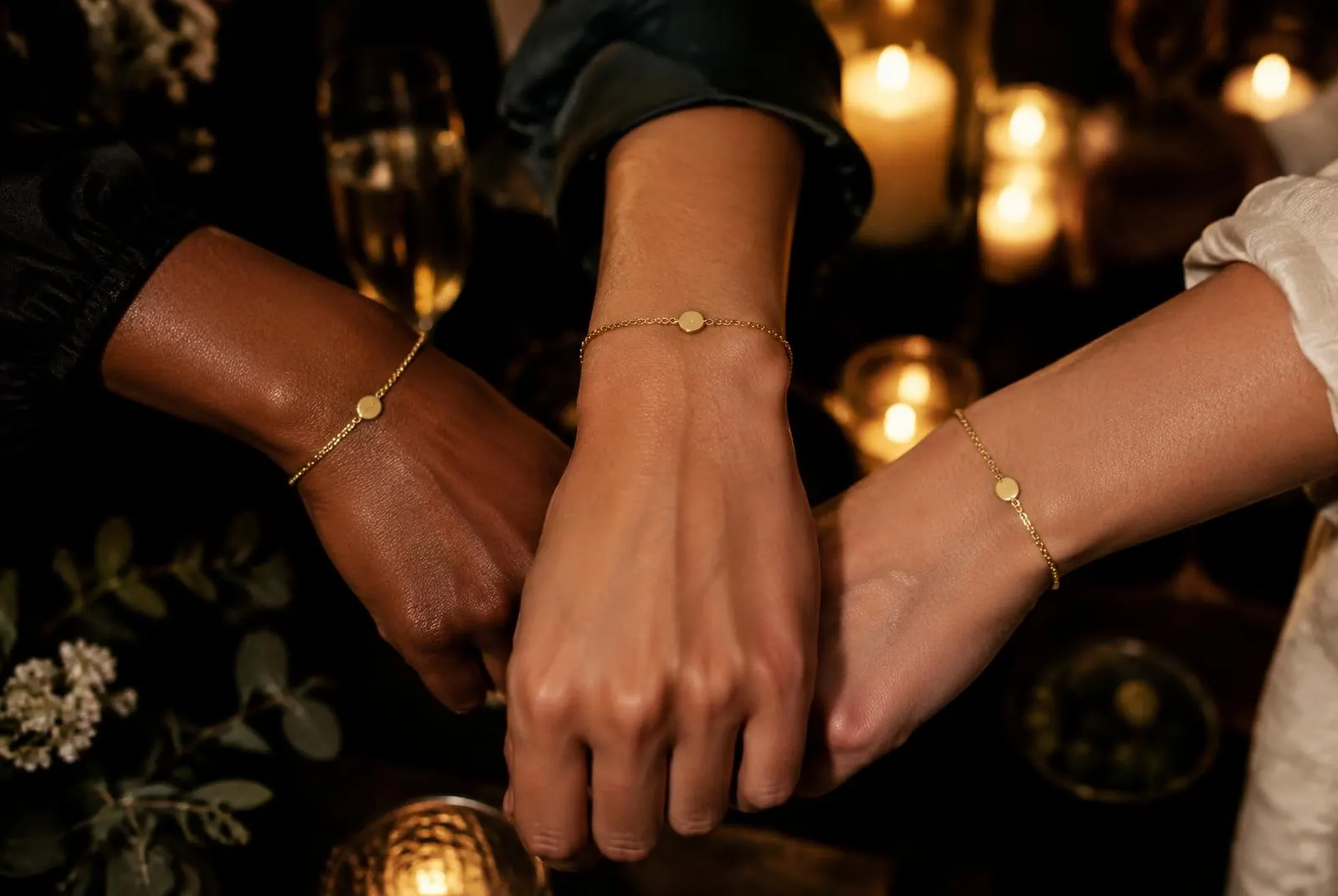 Friends' wrists with matching gold bracelets at an evening gathering